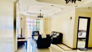 A spacious living room with a black leather sofa, a small table, and a chandelier. - Near the ocean  with Swimming pool ,Supermarket and ATM machine at the premises. (Dar es Salaam)