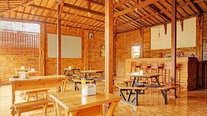 A rustic wooden interior with multiple picnic tables and benches, a wooden ceiling, and a simple kitchen area. - OYO Life 92568 Penginapan Joglo Syariah (Kepanjen)