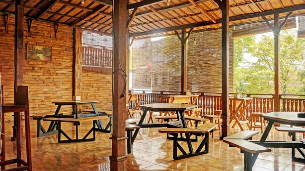 An outdoor wooden pavilion with picnic tables and benches, surrounded by a wooden fence and trees. - OYO Life 92568 Penginapan Joglo Syariah (Kepanjen)