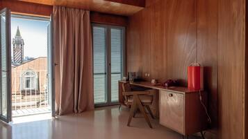 A modern room with a wooden desk, a chair, a red water bottle, and a view of a building through a large window.