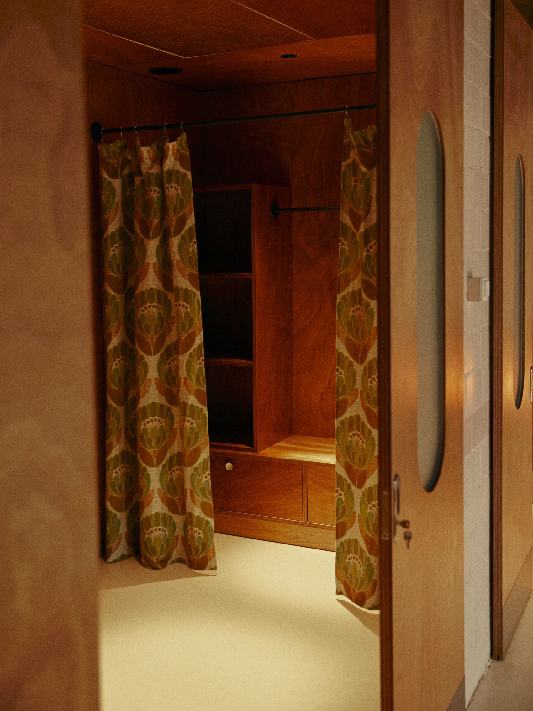 A room with a wooden wardrobe, a small shelf, and a door with a mirror.