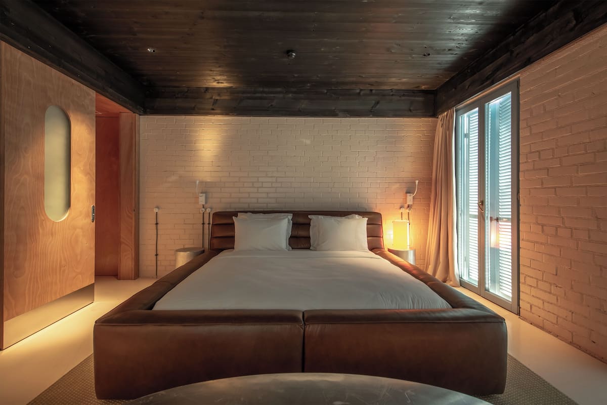 Un dormitorio moderno con una cama grande, techo de madera, paredes de ladrillo y una ventana con persianas.