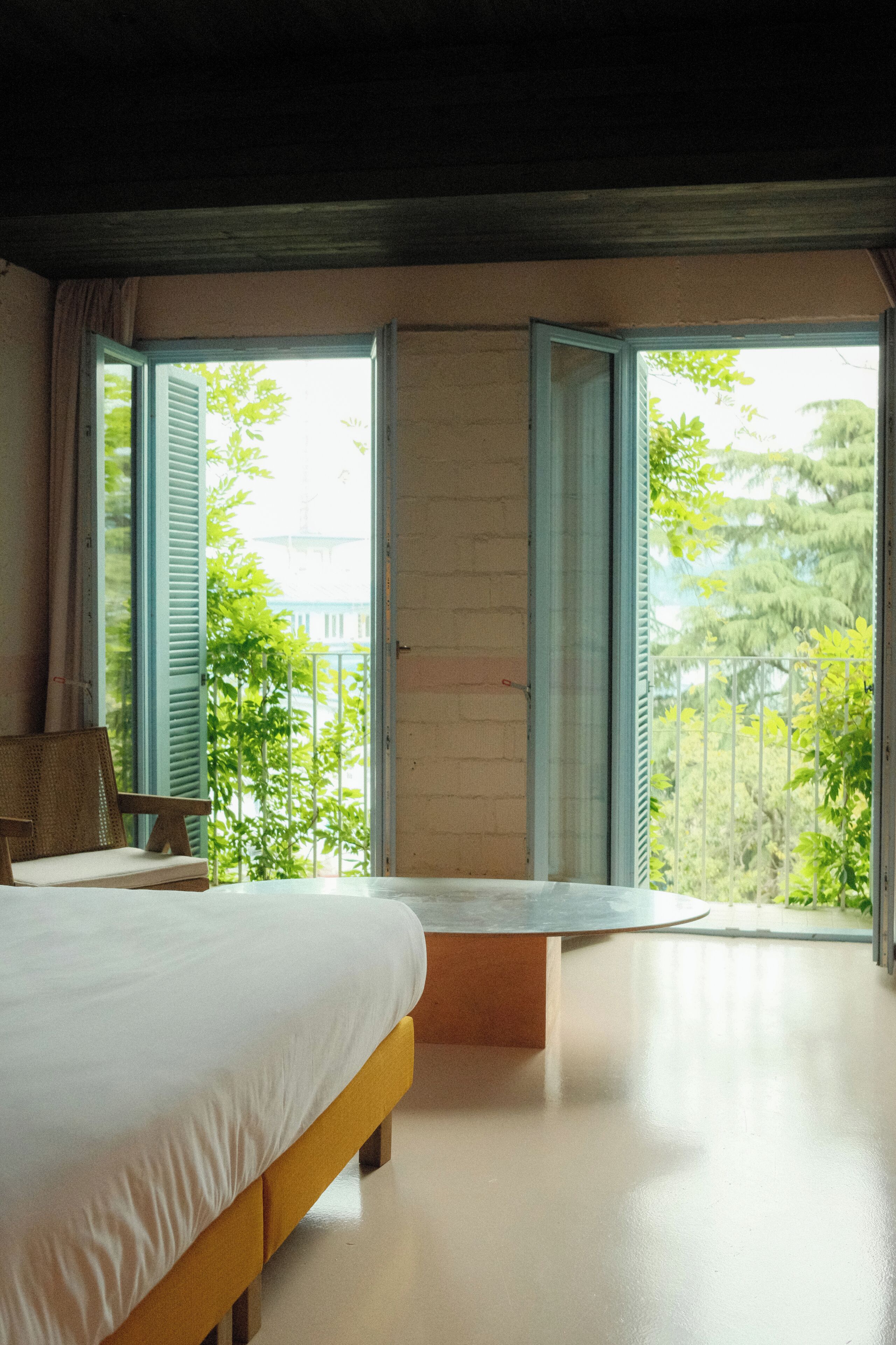 A bedroom with a bed, a chair, and a large window with shutters.