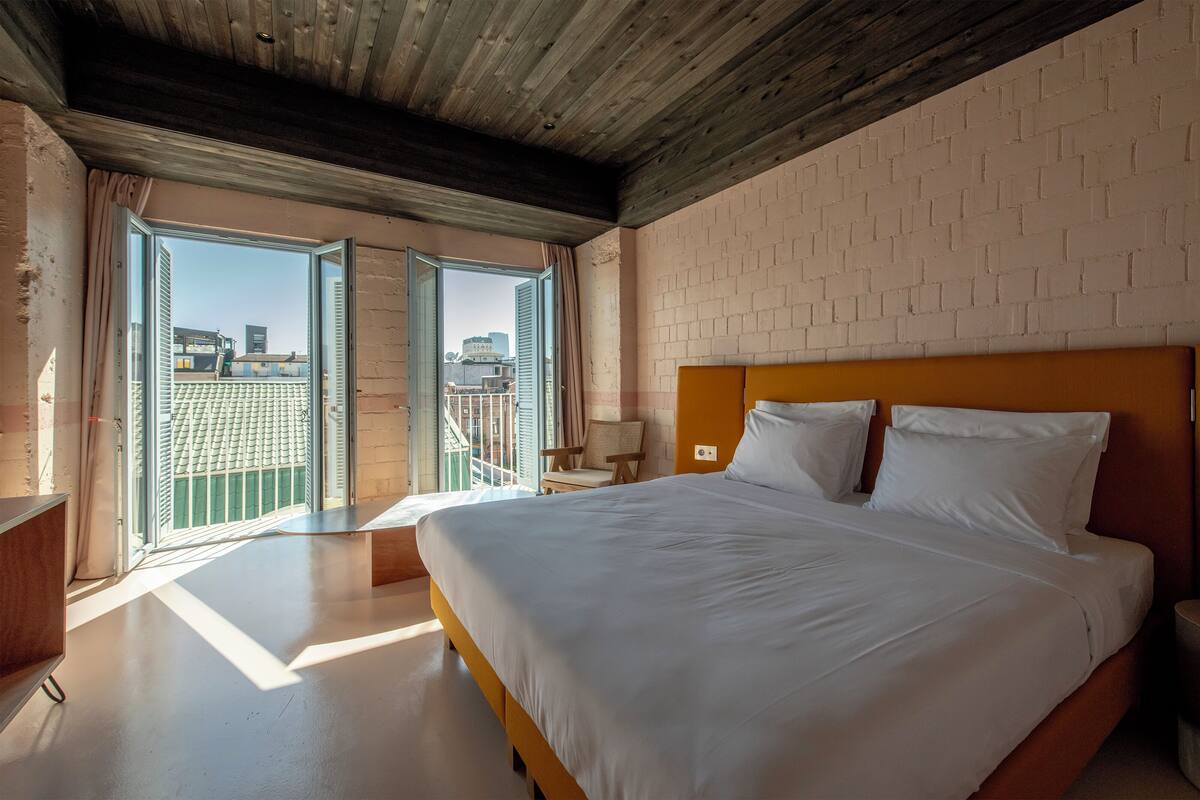 Un dormitorio con una cama grande, cabecera de madera, mesita de noche y vistas a un paisaje urbano a través de una puerta corrediza.