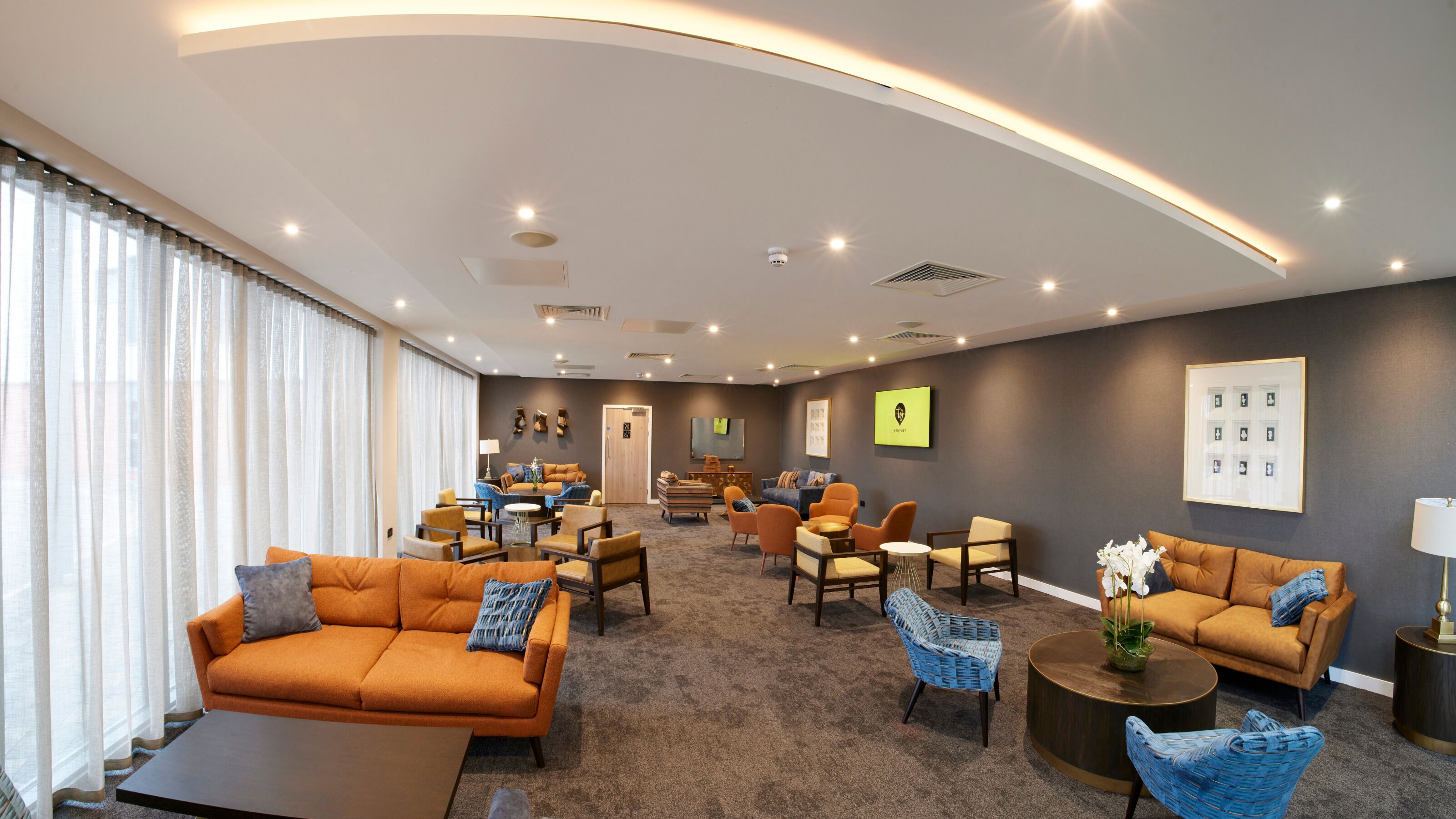 A spacious living area with a large sofa, armchairs, and a coffee table. There are multiple seating options and a television mounted on the wall.