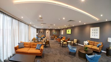 Amplia sala de estar con un sofá grande, sillones y una mesa de centro. Ofrece diversas opciones de asientos y un televisor montado en la pared.