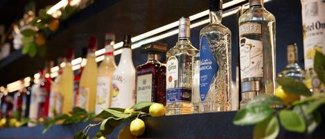 A bar shelf with various liquor bottles, including Antica Sambuca and RONDF, and a decorative plant with lemons.