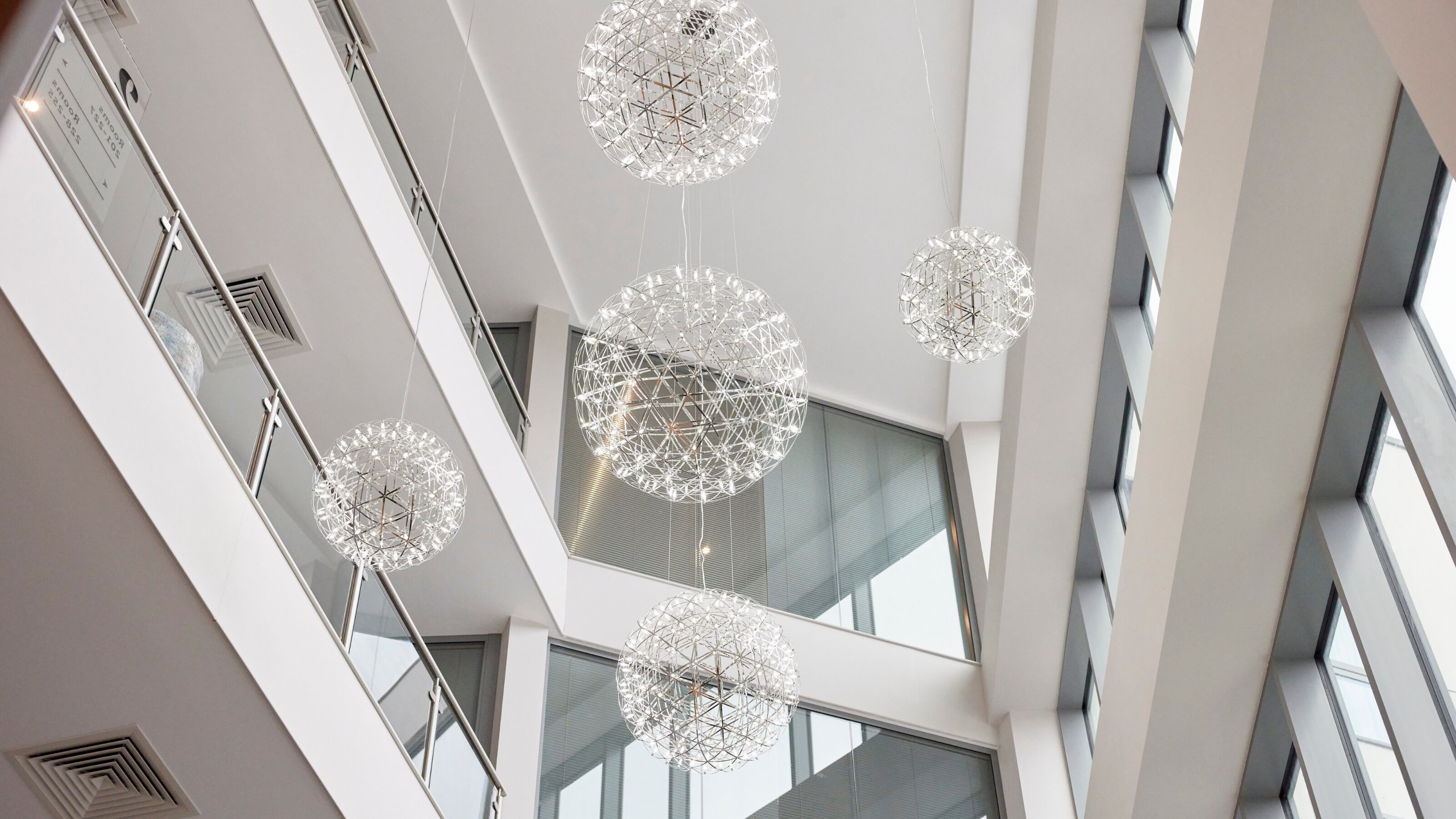 Un intérieur moderne avec de nombreux étages, de grandes fenêtres et des luminaires sphériques suspendus.