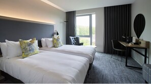 A hotel room with two beds, a desk, a chair, and a large window. - Tŷ Newport (Newport)