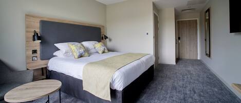 A modern hotel room with a large bed, a bedside table, a chair, and a TV mounted on the wall.