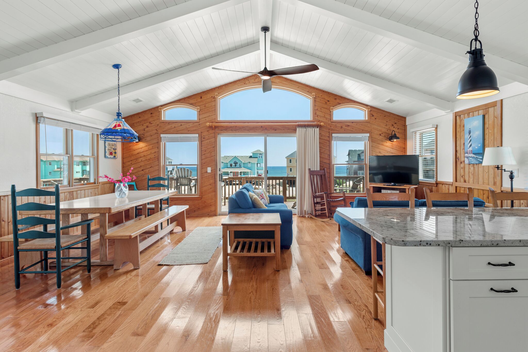 A spacious living area with a wooden ceiling, large windows, a blue sofa, and a TV.