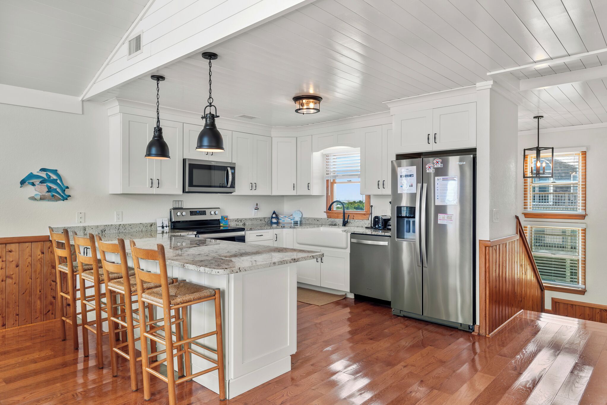 A spacious kitchen with white cabinetry, a stainless steel refrigerator, and a wooden island with bar stools.