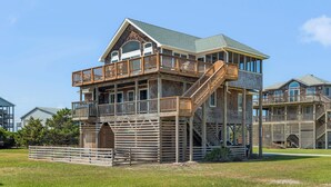 A large, multi-story building with a wooden exterior, multiple balconies, and a central staircase. - In Due Tide: Oceanside, Hot Tub, Dogs OK (Rodanthe)