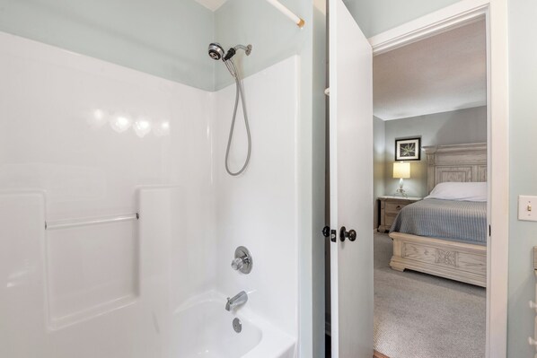 A bathroom with a bathtub, shower, and a door leading to a bedroom with a bed and nightstand. - Blue Paradise Club: Golf Community | Hot Tub (Kitty Hawk)