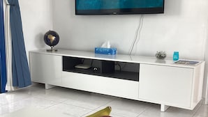 A living room with a TV displaying 'BLUE LAGOON' and a bowl of fruit on the table. -  POOL VIEW APARTMENT WALK TO THE BEACH & HARBOUR (Paphos)