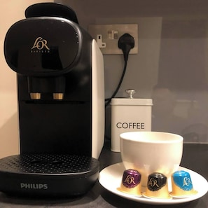 A coffee machine, a coffee container, and a cup with three coffee pods on a table.