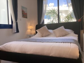 A neatly made bed with white linens and two pillows, a bedside lamp, and a window with curtains.