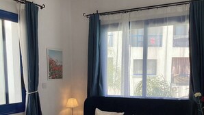 A neatly made bed with a headboard, a bedside lamp, and a view of the outside through a window with curtains. -  POOL VIEW APARTMENT WALK TO THE BEACH & HARBOUR (Paphos)