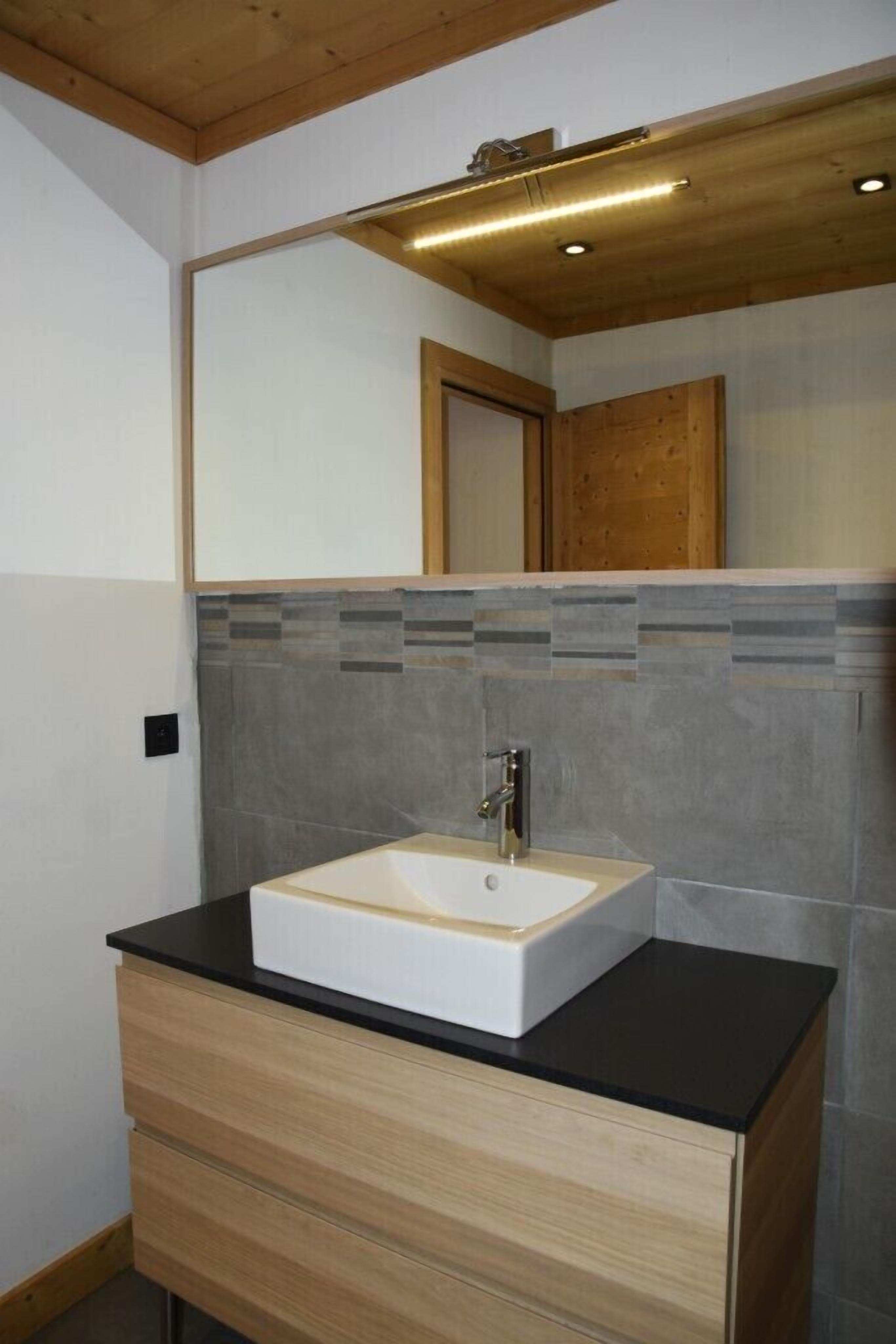 A bathroom with a white sink, wooden vanity, and a mirror with a wooden frame.