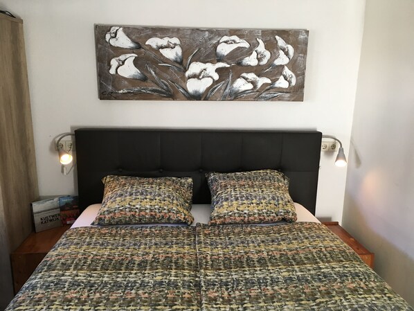 Ein Bett mit einem gemusterten Überwurf, zwei passende Kissen, ein schwarzes möbliertes Kopfteil und ein an der Wand hängendes Blumenbild.