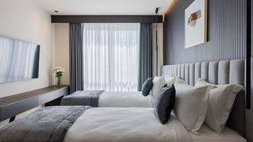 Quarto de hotel moderno com uma cama grande, mesa de cabeceira, TV de tela plana e uma janela ampla com cortinas.