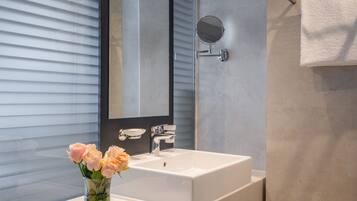 A modern bathroom with a large mirror, a white sink, and a glass vase with flowers.