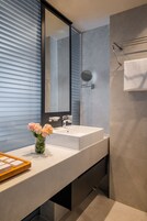 Un baño moderno con un espejo grande, un lavamanos blanco y una florera de cristal con flores.