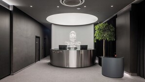 A modern reception desk with a logo, a reception area, and a large potted plant. - Derand Hotel (Pristina)