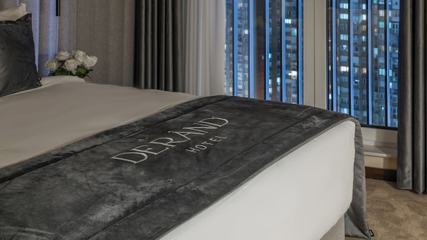 A hotel room with a bed, a nightstand, a vase with flowers, and a view of the city at night. - Derand Hotel (Pristina)