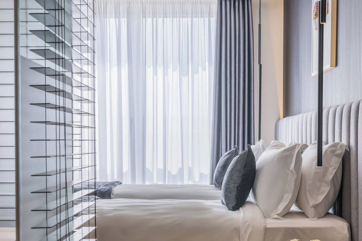 A modern hotel room with a large bed, a bedside table with a vase of flowers, and a view of the city through the window.