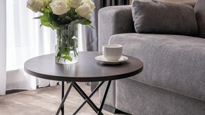 A modern living room with a grey sofa, a round coffee table with a white cup, and a vase of white roses. - Derand Hotel (Pristina)