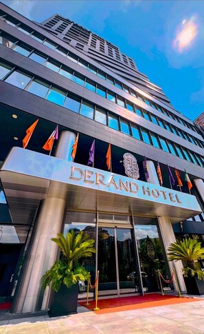 Un hôtel moderne, reconnaissable à son enseigne bien visible où l’on peut lire « DERAND HOTEL ».