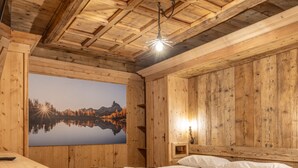 A wooden cabin room with a bed, a painting of a lake, and a small table. - Casa Aquila, with sauna and Turkish bath (Cortina d´Ampezzo)