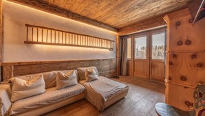 A cozy room with a wooden ceiling, a sofa with cushions, a wooden cabinet, and a window with a view of trees. - Casa Aquila, with sauna and Turkish bath (Cortina d´Ampezzo)