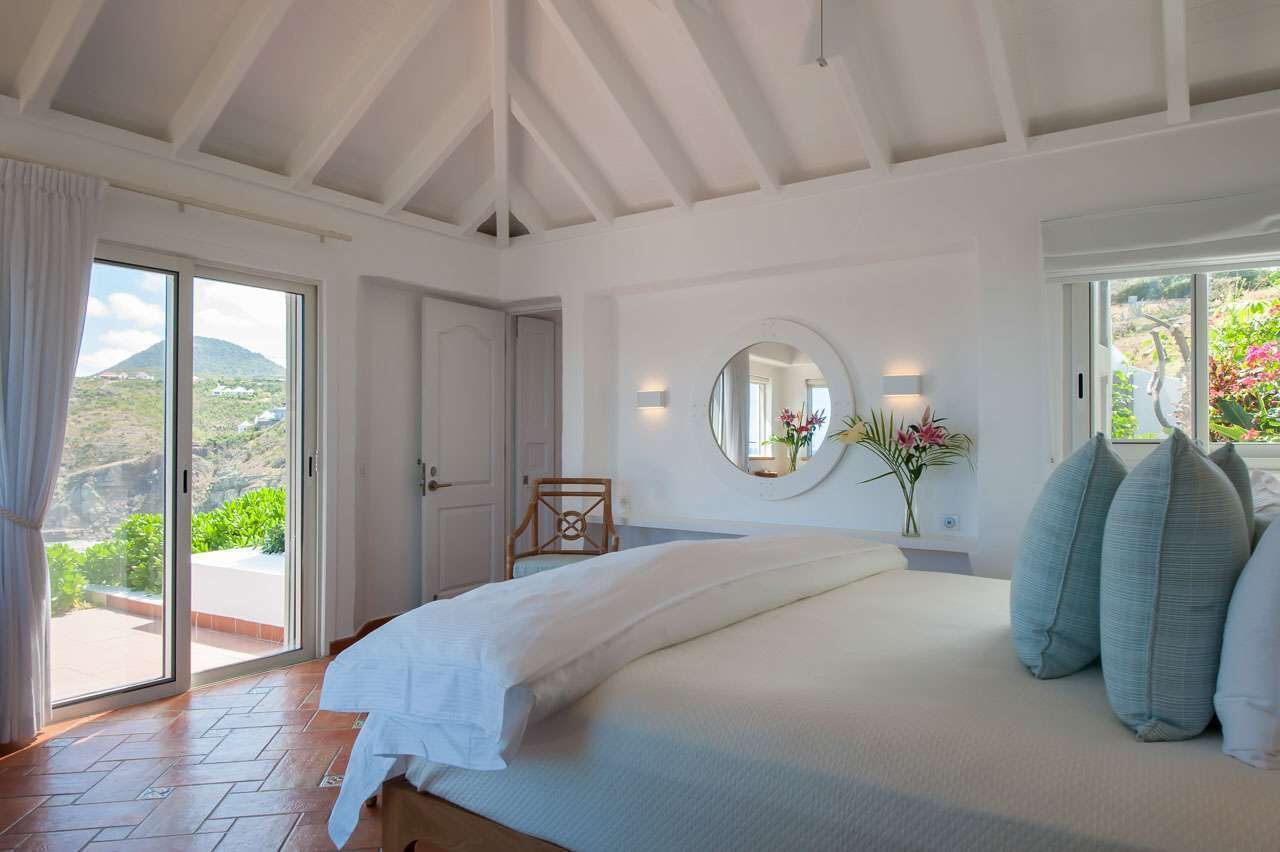 Une chambre avec un grand lit, un miroir rond et une vue sur la verdure.
