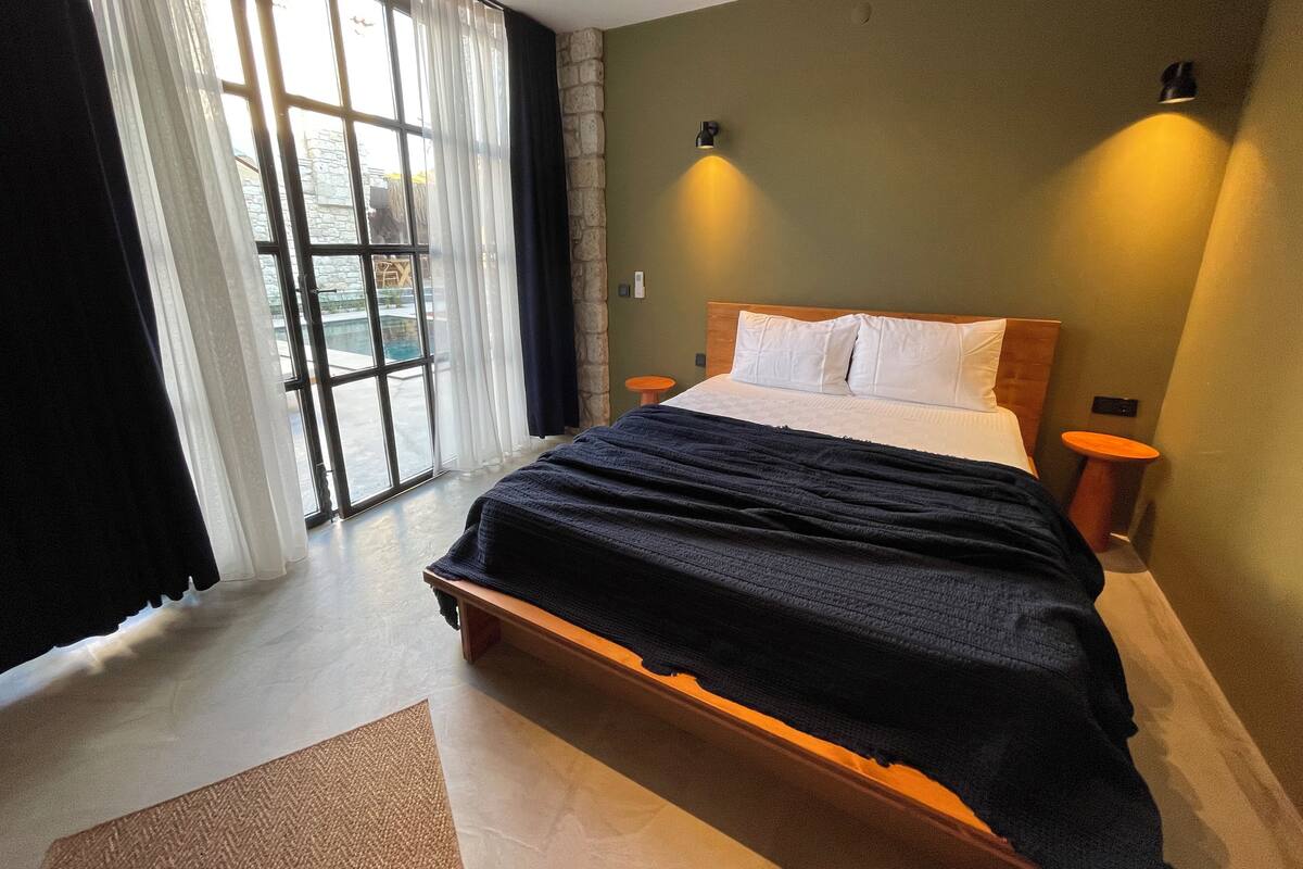 Un dormitorio con una cama grande, dos mesitas de noche, vista a una piscina a través de una puerta corrediza de vidrio y una pared de acento de piedra.