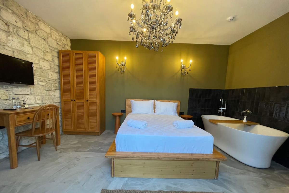 Un dormitorio con cama de madera, un escritorio con silla, televisor, candelabro y bañera.