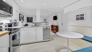 Une cuisine moderne avec des meubles blancs, un four encastré et un lave-vaisselle. On y trouve également un coin repas avec une table blanche et un banc rembourré bleu.