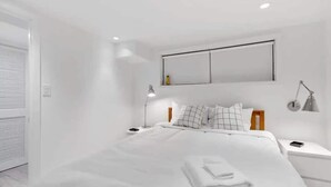 Une chambre moderne avec un grand lit, du linge de lit blanc, une table de chevet avec une lampe et un téléviseur fixé au mur.