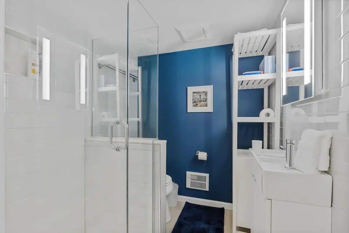 Ein modernes Badezimmer mit Duschkabine aus Glas, blauer Akzentwand und weißen Sanitärobjekten.