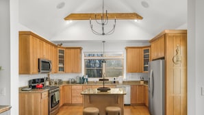 A modern kitchen with wooden cabinets, stainless steel appliances, and a central island with stools. - Stunning Views, Hot Tub, Impeccable Design (Wintergreen Resort)