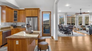 A spacious kitchen with wooden cabinets, a central island, and a dining area with a view of the outdoors. - Stunning Views, Hot Tub, Impeccable Design (Wintergreen Resort)