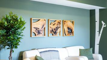 A modern living room with a white sofa, a green plant, and three abstract wooden art pieces on the wall.
