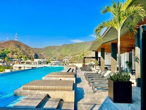 A poolside area with lounge chairs and a view of a mountain and buildings in the distance. - New Boho Chic Studio! Madero 320! (Puerto Vallarta)
