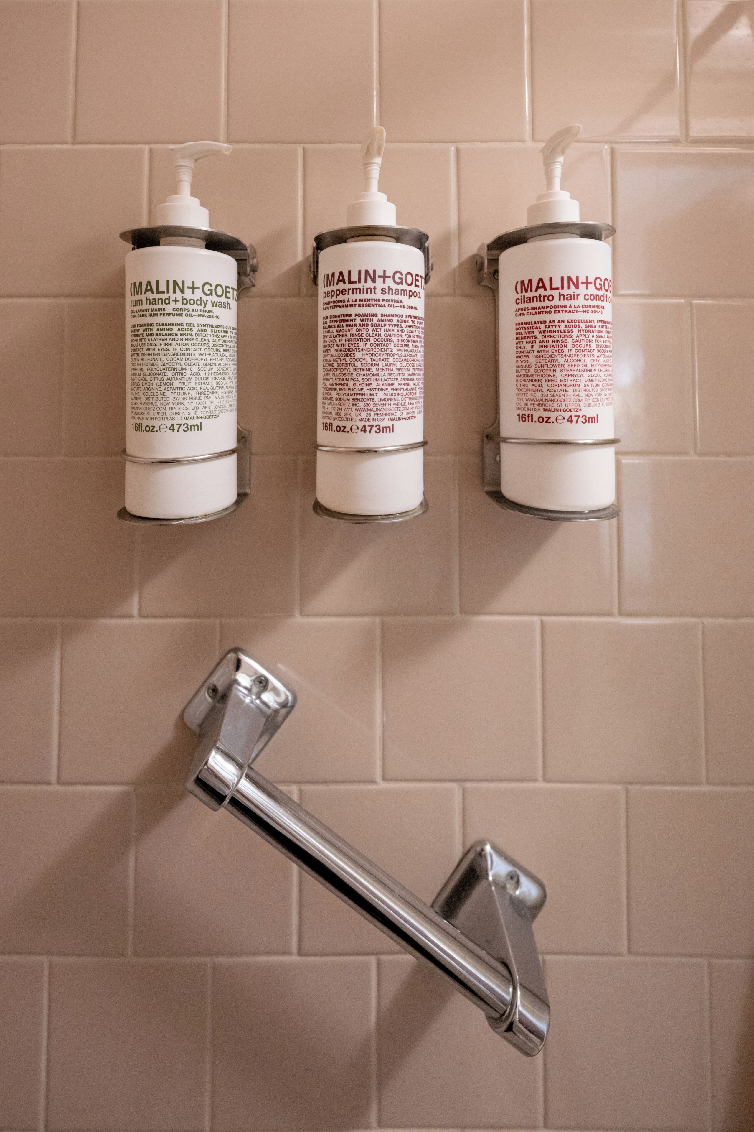 Three toiletry bottles mounted on a wall with a chrome faucet below.