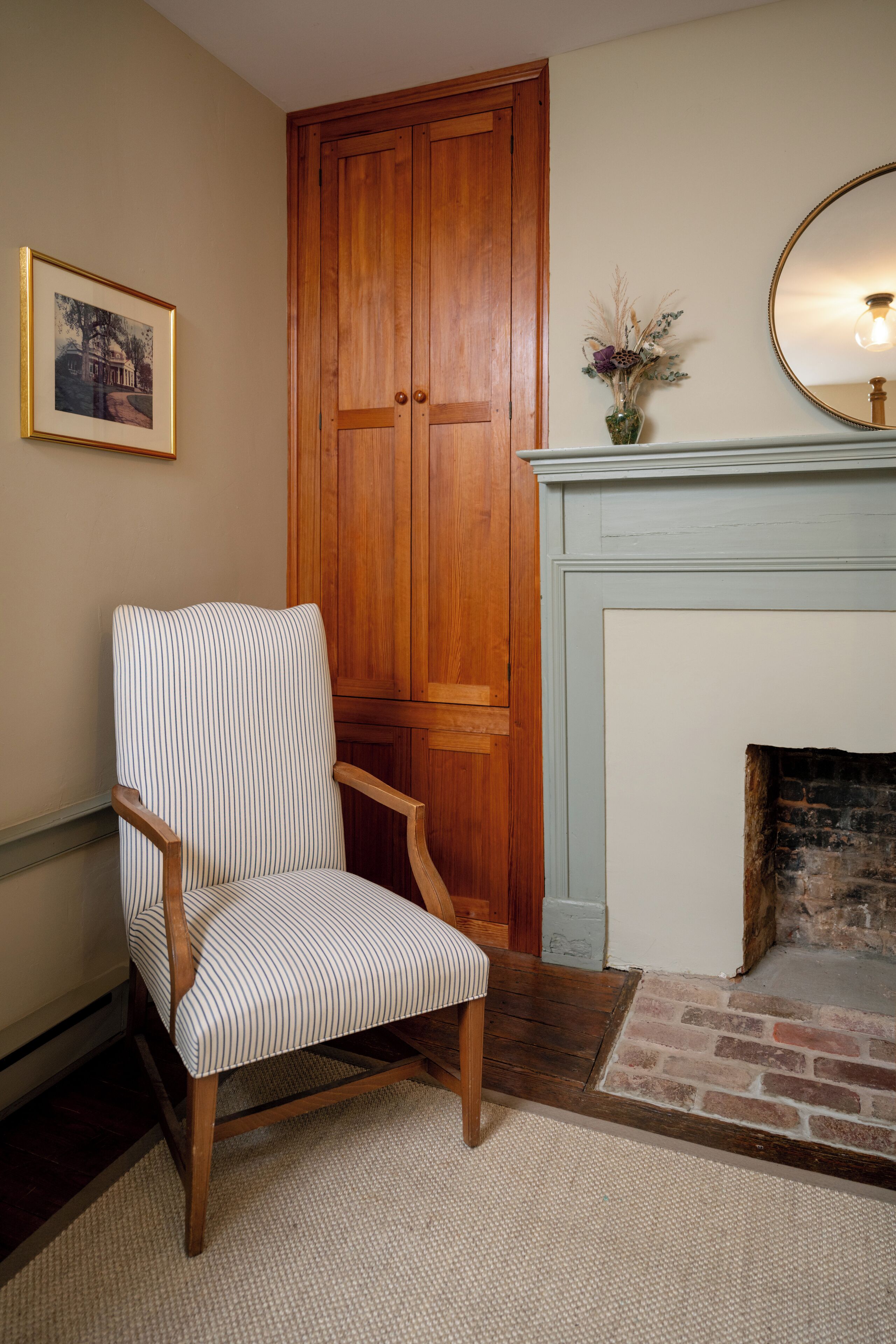 A room with a wooden chair, a fireplace, and a framed picture on the wall.