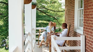 A covered porch with white railings, brick walls, and hanging planters. - The Crossroads Inn (North Garden)