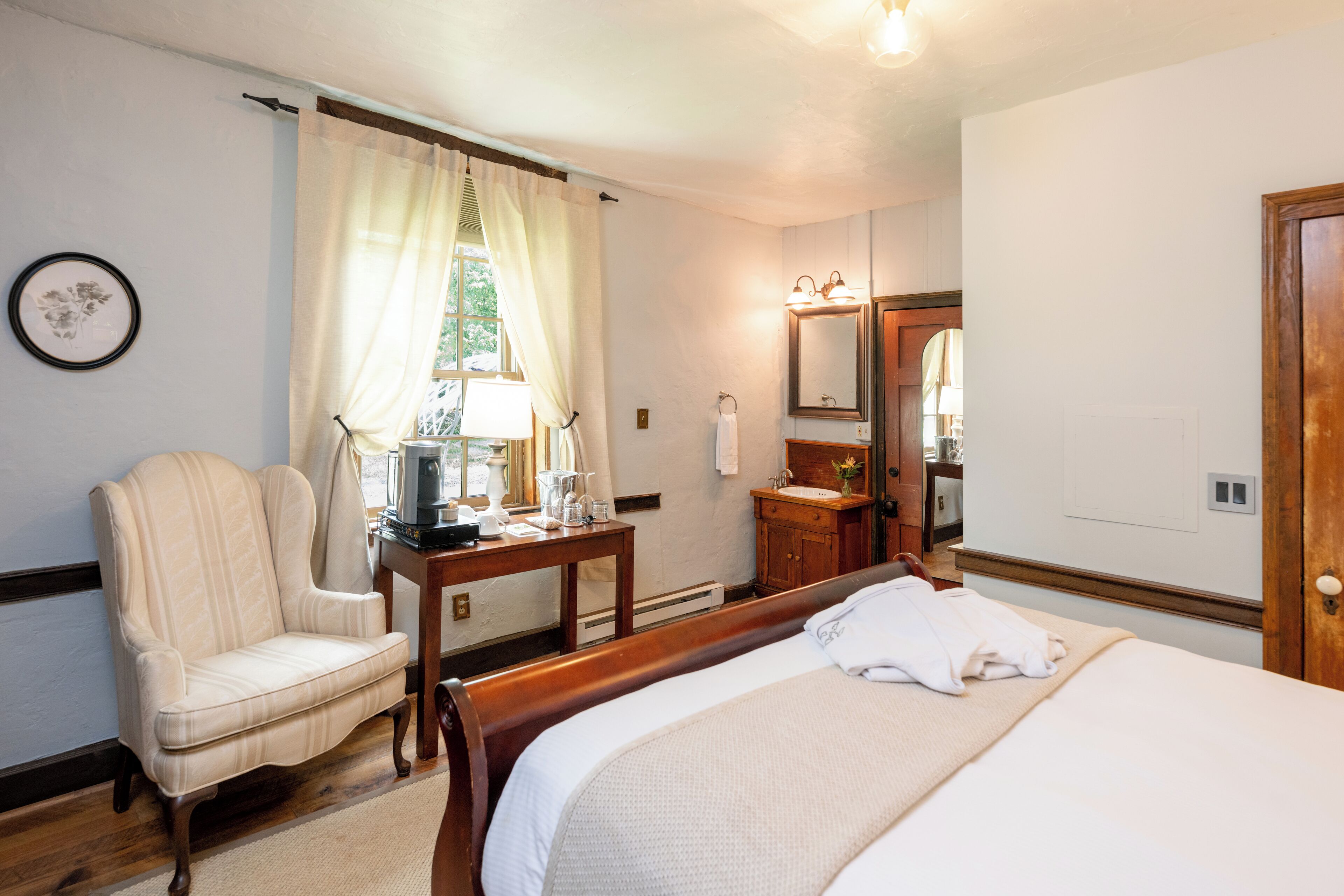 A hotel room with a bed, a chair, a table with a lamp, a sink, and a mirror.