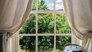 A room with a large window, a table with teapots, cups, and a kettle, and a view of greenery outside. - The Crossroads Inn (North Garden)