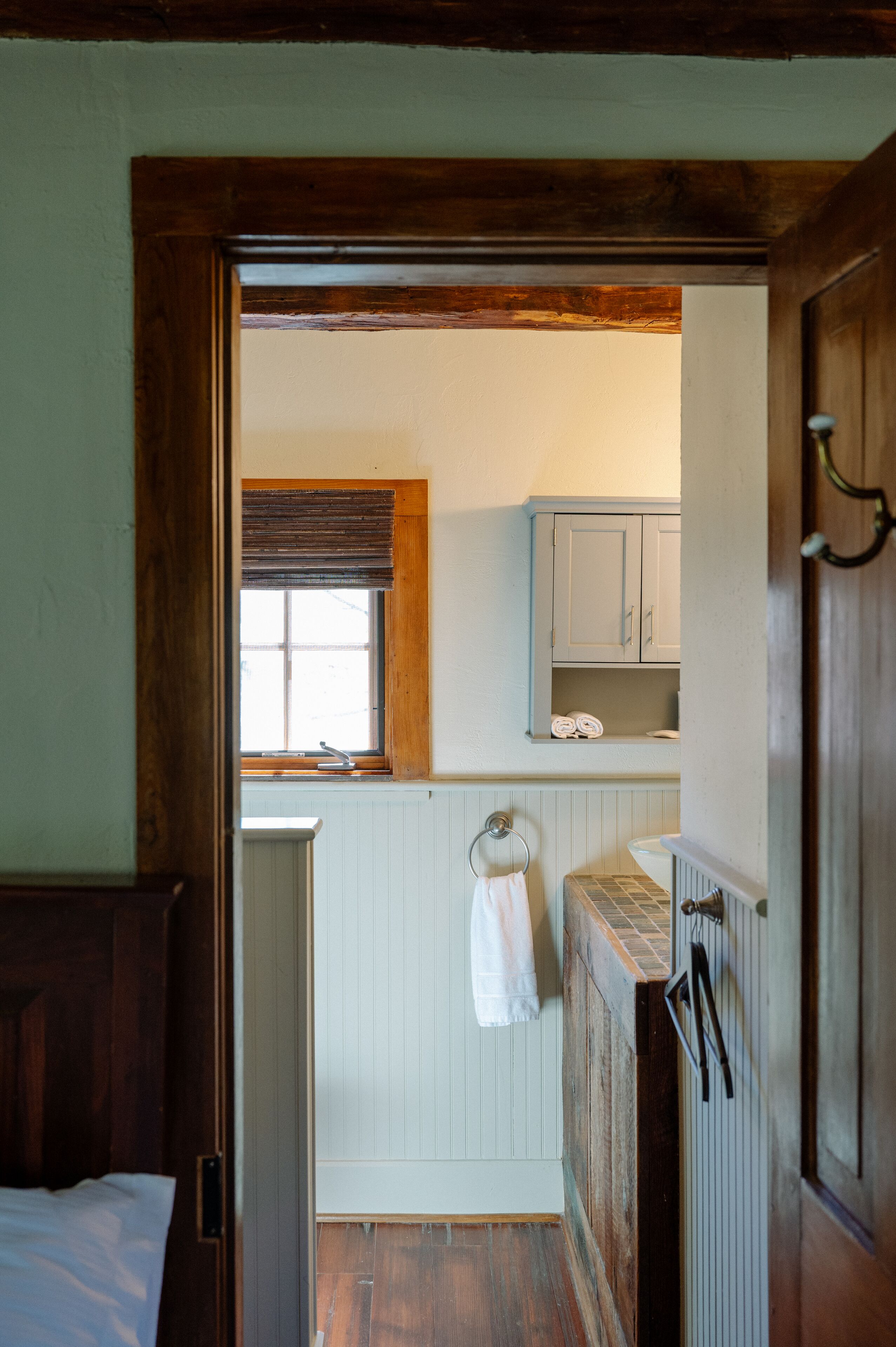 A narrow hallway leading to a bathroom with a window, wooden door, and a towel hanging on a radiator.